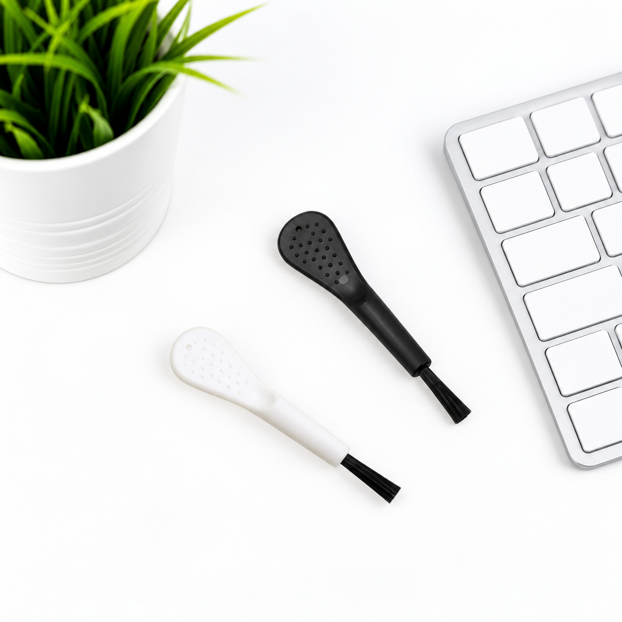 Retouched desktop scene with two mini dusting brushes, a generic keyboard and a plant