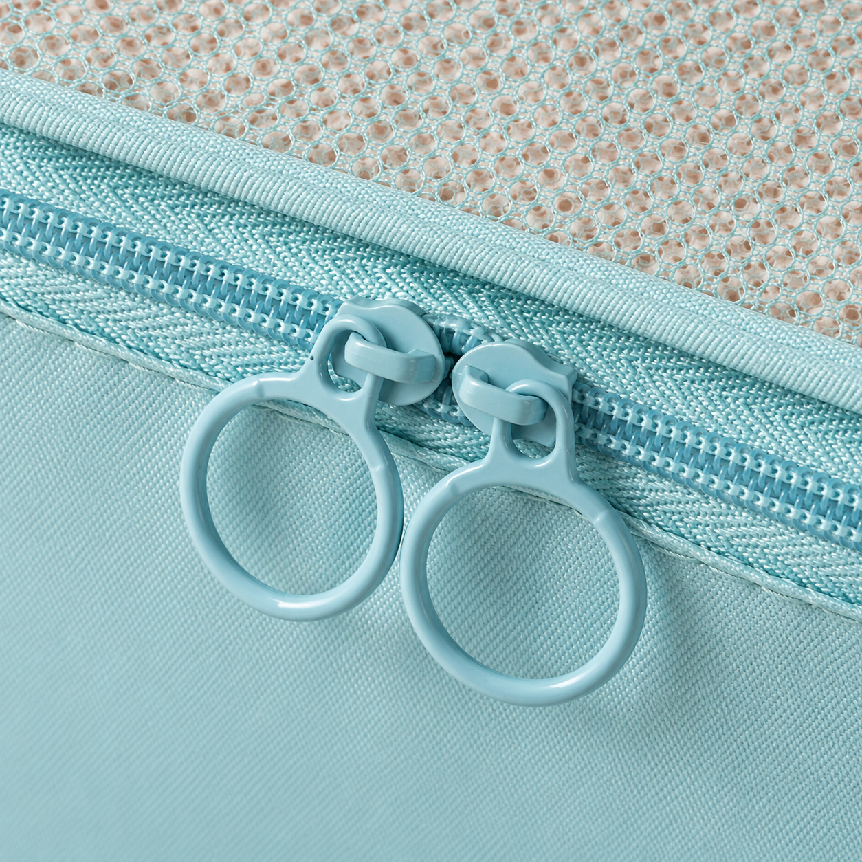 Retouched close-up of circular zipper pulls on a lake-blue mesh packing cube